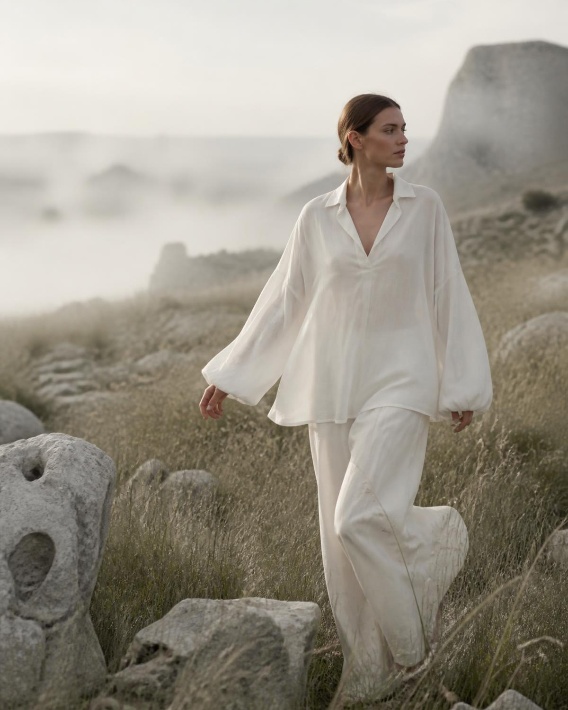 Woman in flowing white linen walking through a limestone meadow at dawn
